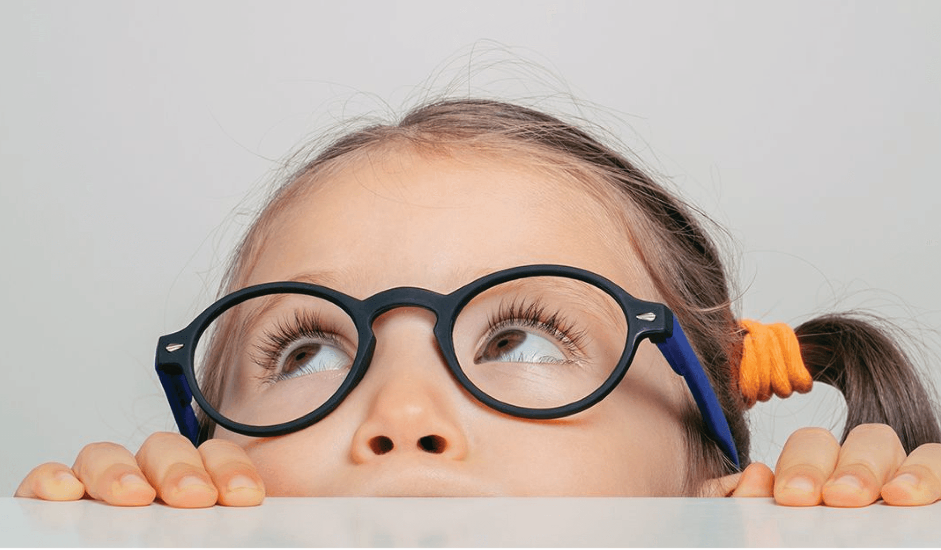 Child wearing glasses and looking up over the edge of a table